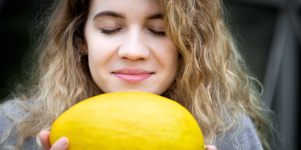 Young woman is smelling a yellow melon with her eyes closed